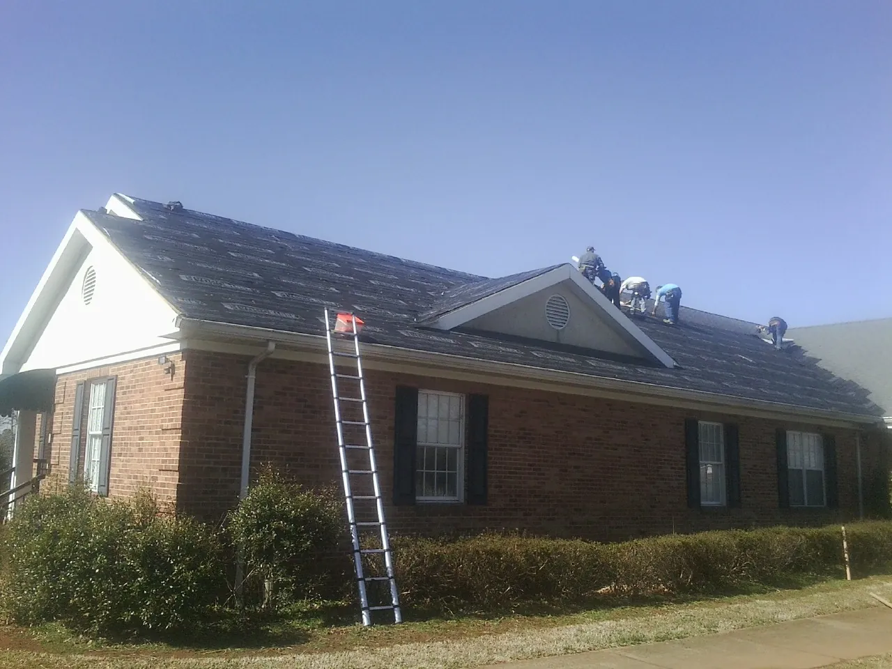 Crew tearing shingles off a brick ranch roof with a ladder set — Metal Roof Repair work by our crew in Moss Beach