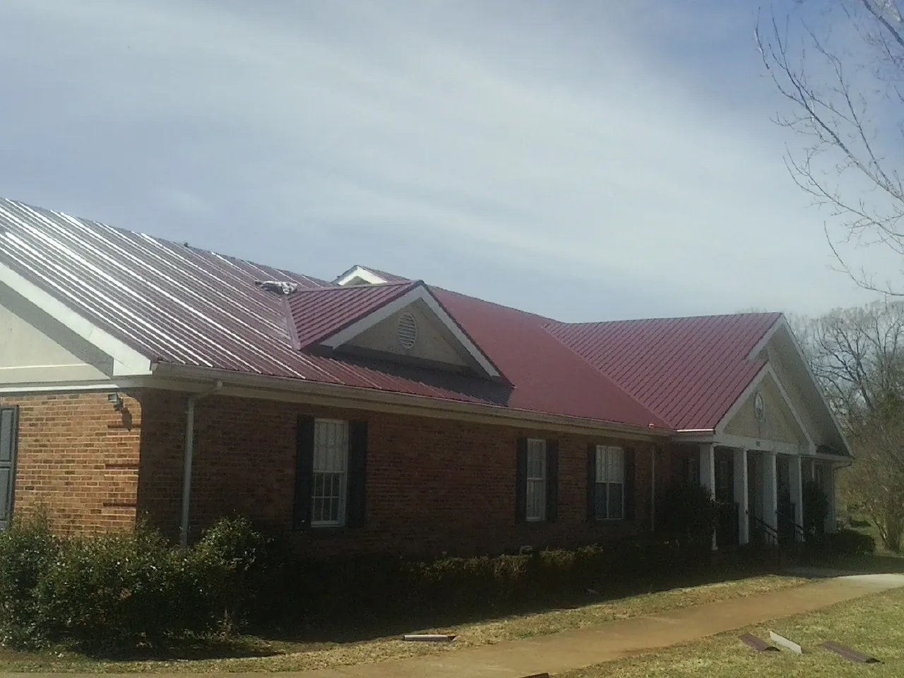 Red metal roof with gabled entries on a long brick building, from a Hail Damage Roof Repair job in Moss Beach