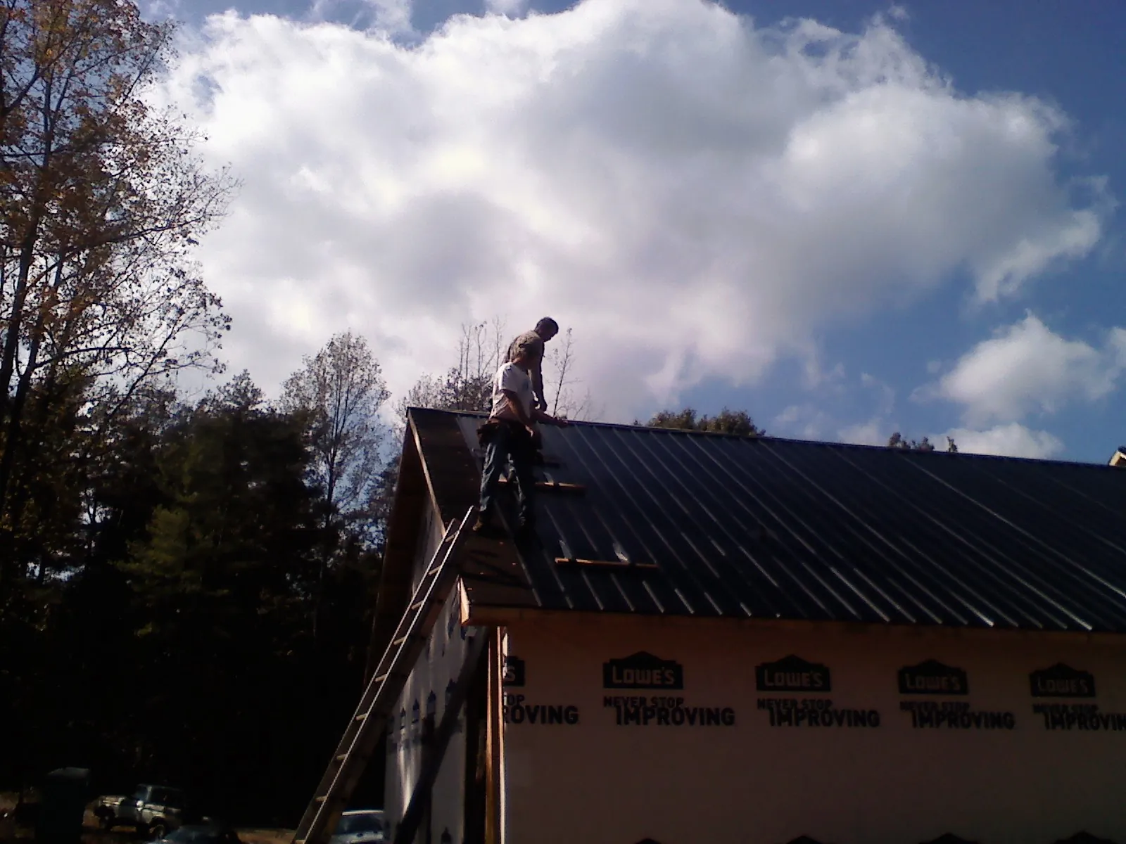 Roofer fastening dark metal panels high against a cloudy sky, from a Roof Inspection job in Moss Beach