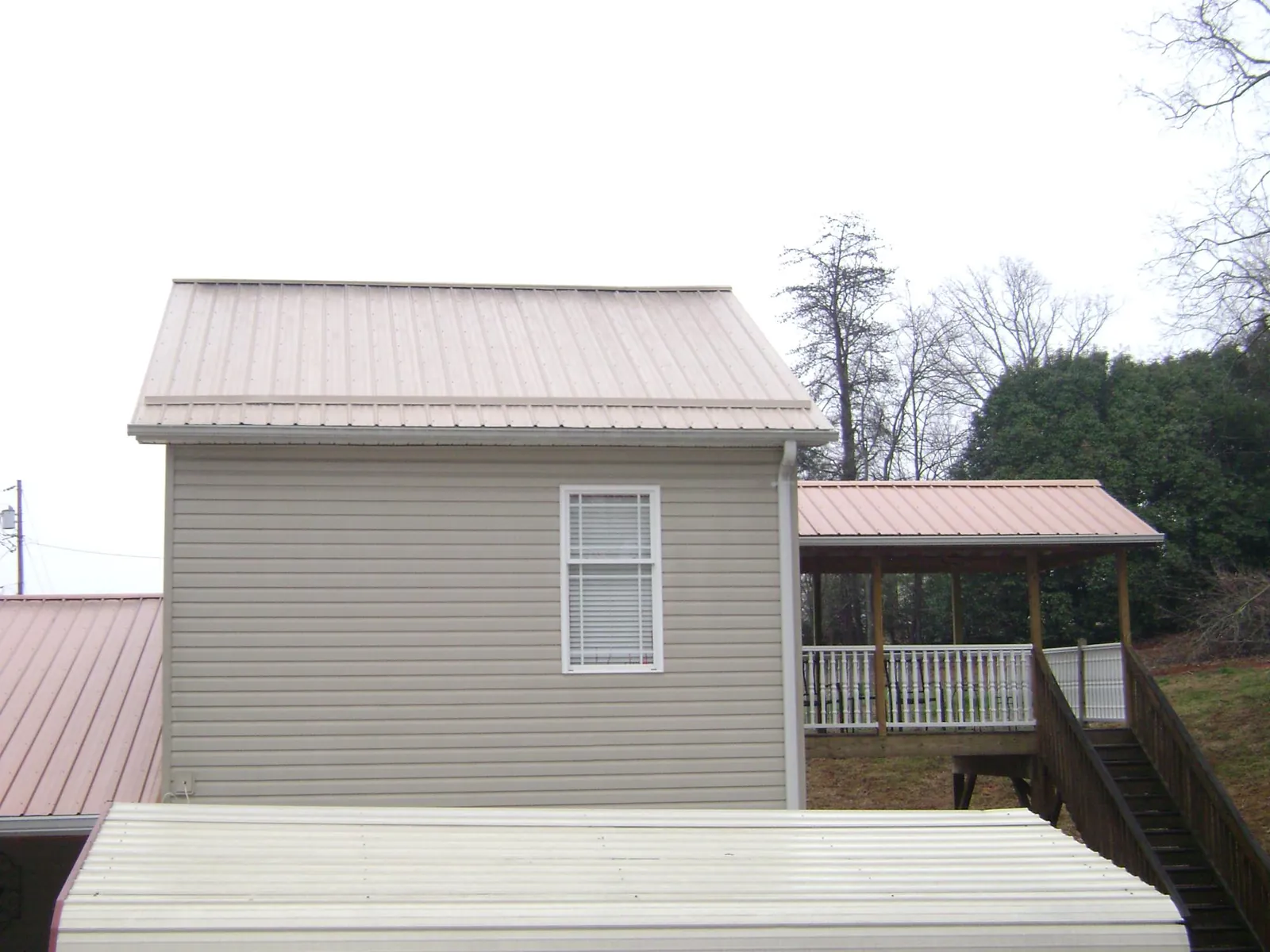 Tan metal roofs on a two story addition and attached porch, from a Roof Replacement job in Moss Beach